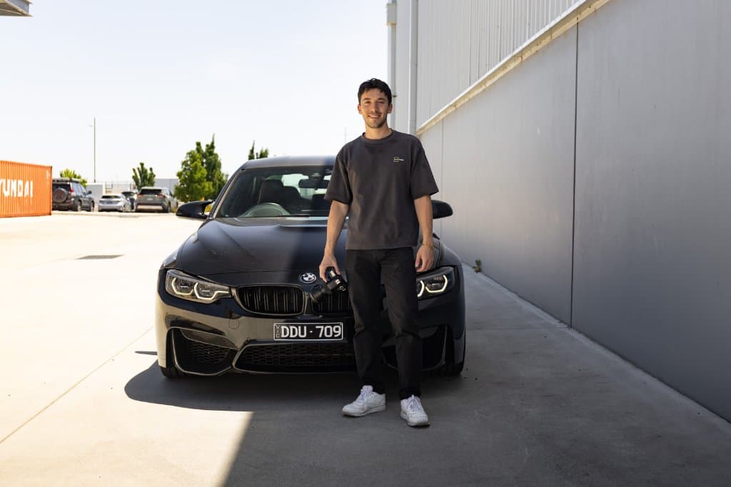 A member of the SCRM Media team with a camera beside a black BMW on a dealership lot